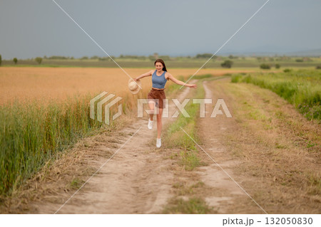 Young woman joyfully runs along a dirt path in a golden field during a sunny day Young woman joyfully runs along a dirt path in a golden field during a sunny day 132050830