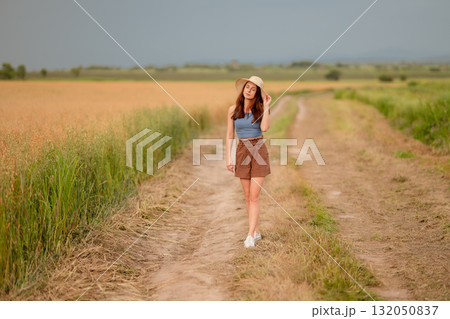 Young woman walks along a dirt path in a vast golden field during a summer afternoon Young woman walks along a dirt path in a vast golden field during a summer afternoon 132050837