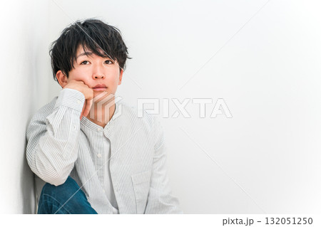 頬杖をつきながらぼんやりと遠くを見つめる若いアジア人男性 頬杖をつきながらぼんやりと遠くを見つめる若いアジア人男性 132051250