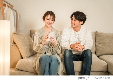 家のリビングのソファーでスマホを見ながら談笑する若いアジア人夫婦,カップル 家のリビングのソファーでスマホを見ながら談笑する若いアジア人夫婦,カップル 132054486