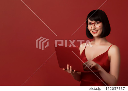 smiling lady in glasses, red dress working on red laptop on red background 132057587