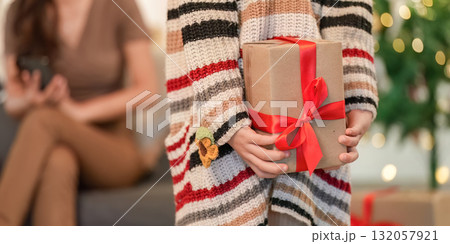 Christmas Gift Exchange. Child presenting a wrapped present to a joyful woman in festive attire. 132057921