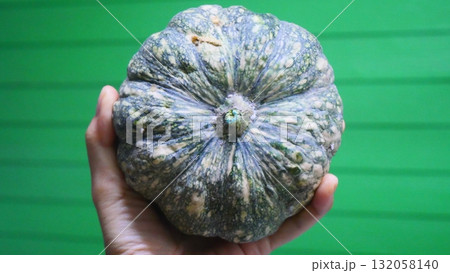 Hand Holding a Small Pumpkin Against a Green Background Hand Holding a Small Pumpkin Against a Green Background 132058140