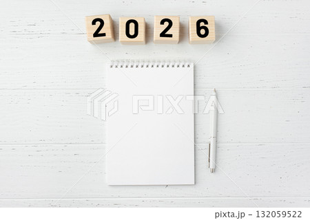 Wooden cubes with numbers for the New Year 2026 with a notebook and pen on a white wooden background 132059522