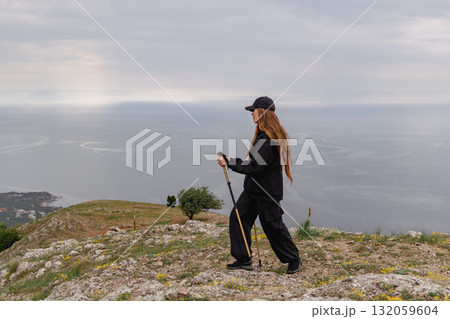 A woman is walking on a hill with a stick and a hat on A woman is walking on a hill with a stick and a hat on 132059604