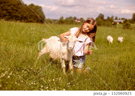 Girl cradling a baby goat in her arms, surrounded by a lush green field, basking in the warmth of a sunny day Girl cradling a baby goat in her arms, surrounded by a lush green field, basking in the warmth of a sunny day 132060925