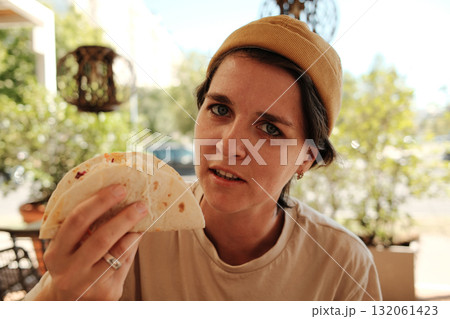 Young woman in yellow beanie holding a taco and looking at camera in Mexican cafe 132061423
