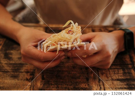 Close-up of woman holding a cheesy taco with both hands at a rustic wooden table 132061424