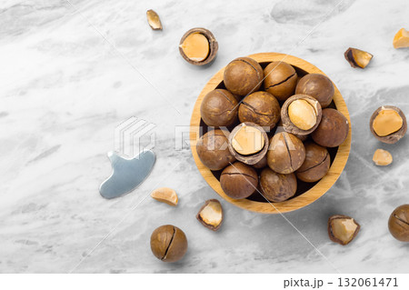 Macadamia nuts with shell  in wood bowl with cracked macadamia on marble table background, top view 132061471