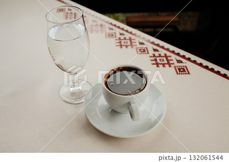 White porcelain cup with strong Turkish black coffee or americano and glass of water served on an outdoor cafe table in natural light White porcelain cup with strong Turkish black coffee or americano and glass of water served on an outdoor cafe table in natural light 132061544