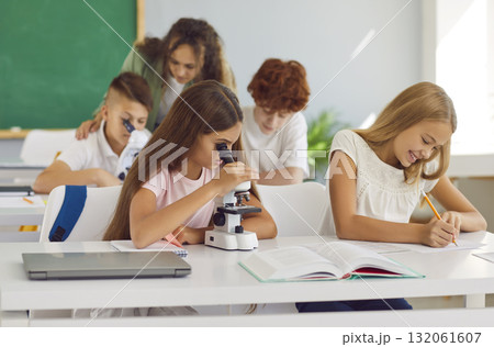 A schoolgirl looking through a microscope during a lesson in classroom. A schoolgirl looking through a microscope during a lesson in classroom. 132061607