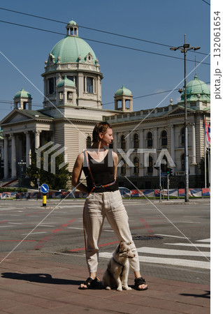 Woman standing with her red merle Border Collie puppy in front of the National Assembly building in Belgrade, Serbia. Front view. Travel with pet concept 132061654