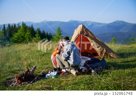 Scenic mountain campsite with two tents in morning. Two campers enjoying serene view of rolling mountains under clear sky. Picturesque sunrise landscape, creating tranquil and cozy outdoor experience. 132061748