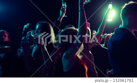 Midnight New Year celebration with people dancing and raising glasses 132061781