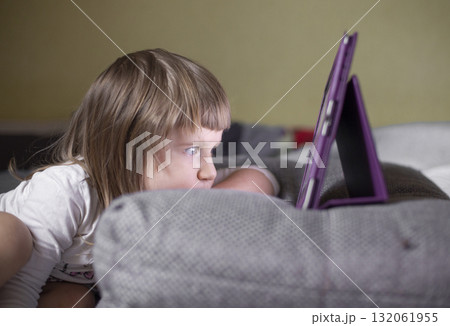 The girl looks at the tablet, which is on the pillow The girl looks at the tablet, which is on the pillow 132061955
