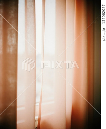 Sunlight streams softly through sheer peach and beige curtains hanging near a window, creating a warm, inviting atmosphere in a tranquil space Generative AI 132062027