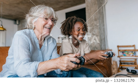 White grandmother and black granddaughter joyfully playing video games together, showcasing multigenerational bonding and emotional connection in family life White grandmother and black granddaughter joyfully playing video games together, showcasing multigenerational bonding and emotional connection in family life 132062170