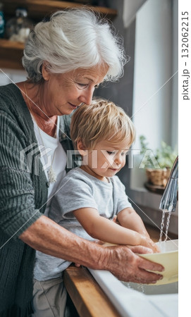Grandmother and toddler joyfully washing dishes together in a cozy kitchen, showcasing multigenerational family life and emotional connection 132062215