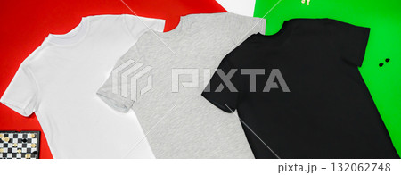 Close-up of the three t-shirts (black, white and grey) on color background redand green. Close-up of the three t-shirts (black, white and grey) on color background redand green. 132062748