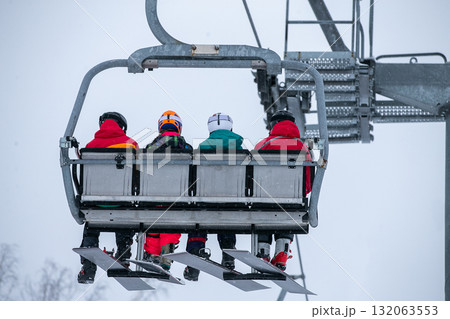 Four female snowboarders on chairlift climb mountain 132063553