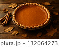 Pumpkin pie with cinnamon sticks and dry autumn leaves on wooden table, traditional fall dessert for Thanksgiving. 132064273