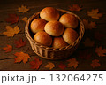 Basket with golden bread rolls on wooden table surrounded by autumn leaves, traditional fall food for Thanksgiving. 132064275
