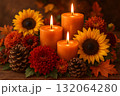 Burning orange candles with sunflowers chrysanthemums pine cones and autumn leaves on wooden table. 132064280