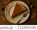 Slice of pumpkin pie on vintage plate, surrounded by autumn leaves and acorns, cozy fall dessert. 132064286