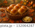 Freshly baked dinner rolls in basket with butter, surrounded by autumn leaves on rustic wooden table. 132064287
