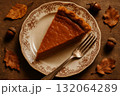 Slice of pumpkin pie on vintage plate with fork, autumn leaves and acorns on wooden table, fall dessert concept. 132064289