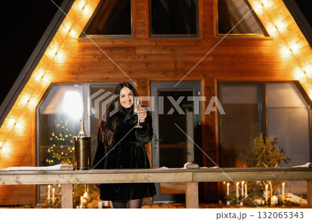 Happy woman celebrating winter holidays drinking champagne in front of her chalet 132065343