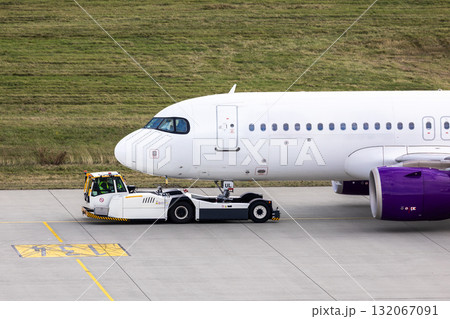 Modern regional jet aircraft towed by ground vehicle on airport taxiway tarmac under sunlight. Engine cockpit clearly visible crew performs technical operations before next scheduled flight airport 132067091