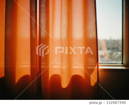 Sunlight streams through sheer red curtains, casting warm, vibrant shadows. The scene is peaceful, highlighting a moment of tranquility in the early morning light Generative AI 132067340