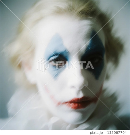 The clown harlequin with pale skin sits quietly, his blue and red face paint accentuating his sadness. Soft lighting creates a moody atmosphere, highlighting his emotions Generative AI 132067794