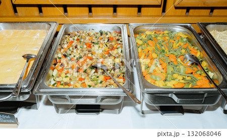 A vibrant buffet setup featuring assorted trays filled with colorful cooked vegetables. Perfect for catering events, showcasing healthy vegetarian options and variety in food presentation 132068046
