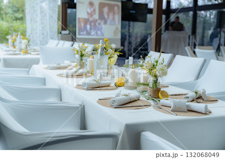 Wedding reception table elegantly set with floral arrangements and candles, creating a sophisticated atmosphere. Plates and cutlery neatly arranged enhance the visual appeal of the setup Wedding reception table elegantly set with floral arrangements and candles, creating a sophisticated atmosphere. Plates and cutlery neatly arranged enhance the visual appeal of the setup 132068049