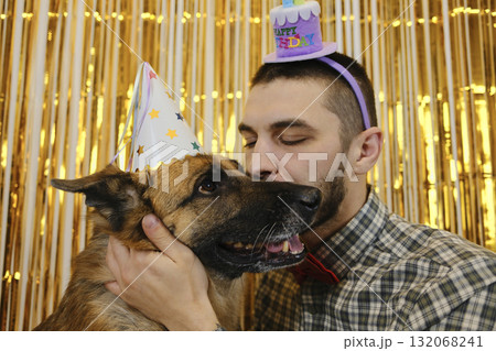 A man in a plaid shirt and bow tie hugs his German Shepherd dog tenderly during a birthday party. Pet birthday party concept 132068241