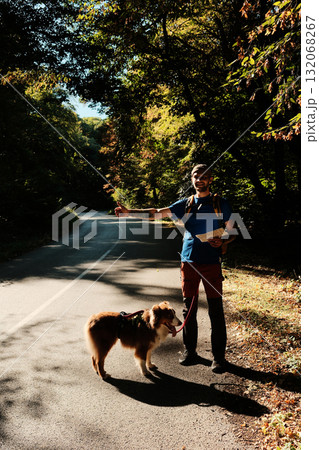 Smiling man with map hitchhiking on a road in forest with his Australian Shepherd dog. Travel with dog concept 132068267