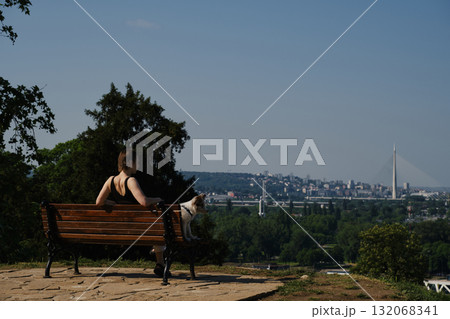 Smiling young woman with her red merle border collie puppy sitting on a bench in Kalemegdan Fortress, Belgrade, with city view in background Smiling young woman with her red merle border collie puppy sitting on a bench in Kalemegdan Fortress, Belgrade, with city view in background 132068341