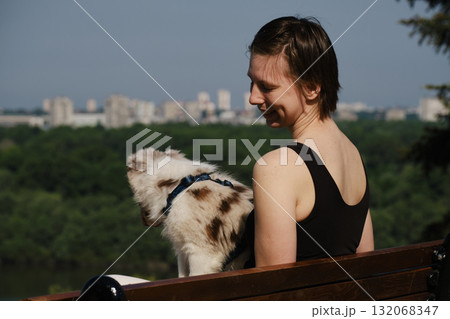 Smiling young woman with her red merle border collie puppy sitting on a bench in Kalemegdan Fortress, Belgrade, with city view in background Smiling young woman with her red merle border collie puppy sitting on a bench in Kalemegdan Fortress, Belgrade, with city view in background 132068347