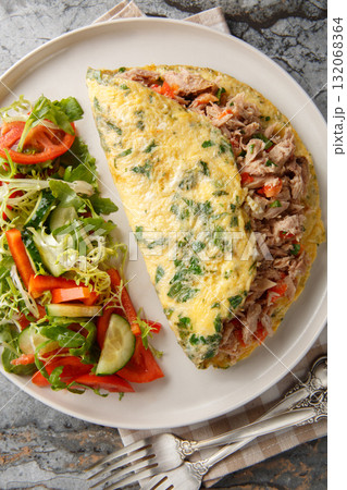 Omelet with canned tuna fish served with fresh vegetables salad closeup on the plate. Vertical top view Omelet with canned tuna fish served with fresh vegetables salad closeup on the plate. Vertical top view 132068364