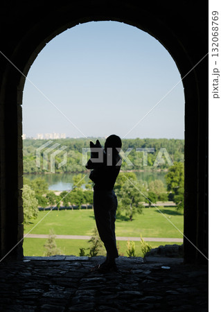Silhouette of a woman holding her red merle Border Collie puppy in arms, standing in stone gate with river and forest view behind Silhouette of a woman holding her red merle Border Collie puppy in arms, standing in stone gate with river and forest view behind 132068769
