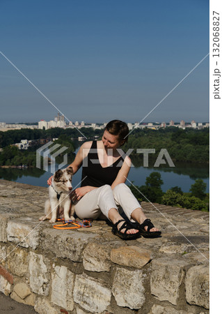Young woman with a red merle Border Collie puppy sitting on stone wall in Kalemegdan Fortress, Belgrade, with city and river view. Travel with dog concept Young woman with a red merle Border Collie puppy sitting on stone wall in Kalemegdan Fortress, Belgrade, with city and river view. Travel with dog concept 132068827