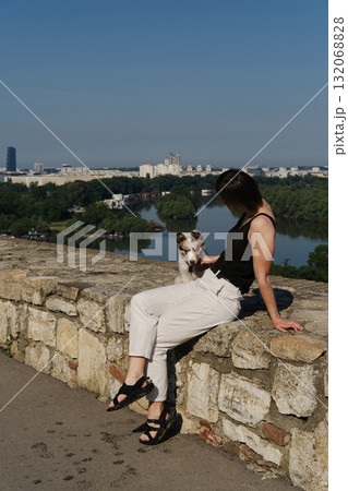 Woman sits with red merle Border Collie puppy on fortress wall at Kalemegdan, overlooking Belgrade city and river. Travel with dog concept Woman sits with red merle Border Collie puppy on fortress wall at Kalemegdan, overlooking Belgrade city and river. Travel with dog concept 132068828