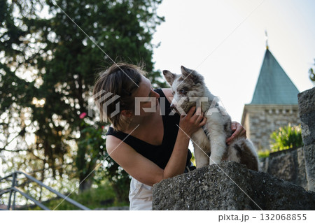 Young woman pets red merle Border Collie puppy on stone wall with sun rays shining through trees, outdoor bonding. Travel with dog concept Young woman pets red merle Border Collie puppy on stone wall with sun rays shining through trees, outdoor bonding. Travel with dog concept 132068855