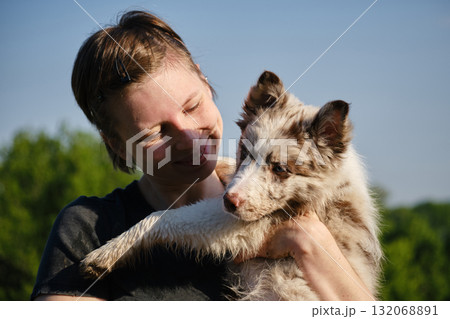 Woman lovingly looks at red merle Border Collie puppy in her arms, sharing an affectionate outdoor moment together 132068891