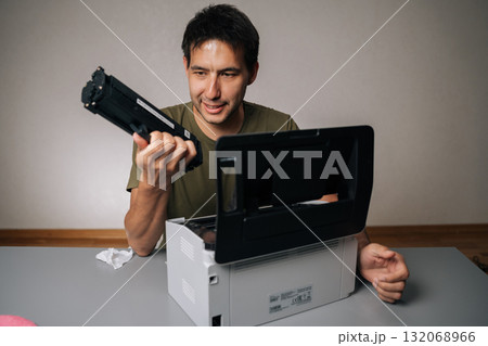 Cheerful computer technician replacing toner cartridge in laser printer during maintenance service, holding new cartridge and looking away, sitting at table on isolated background. 132068966