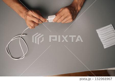 Top view of unrecognizable man connecting USB cable to electronic cigarette charger on gray desk, showcasing charging process of vaping device. Concept of modern alternative to traditional smoking. Top view of unrecognizable man connecting USB cable to electronic cigarette charger on gray desk, showcasing charging process of vaping device. Concept of modern alternative to traditional smoking. 132068967