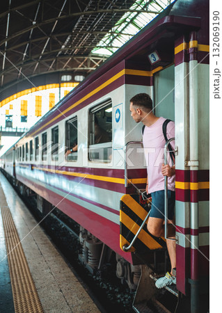 traveler guy boarding train at busy railroad station, young man with backpack starting journey on railway platform traveler guy boarding train at busy railroad station, young man with backpack starting journey on railway platform 132069190