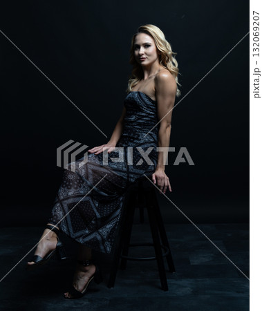 Blond fashion model posing on wooden chair in studio with dark background Blond fashion model posing on wooden chair in studio with dark background 132069207